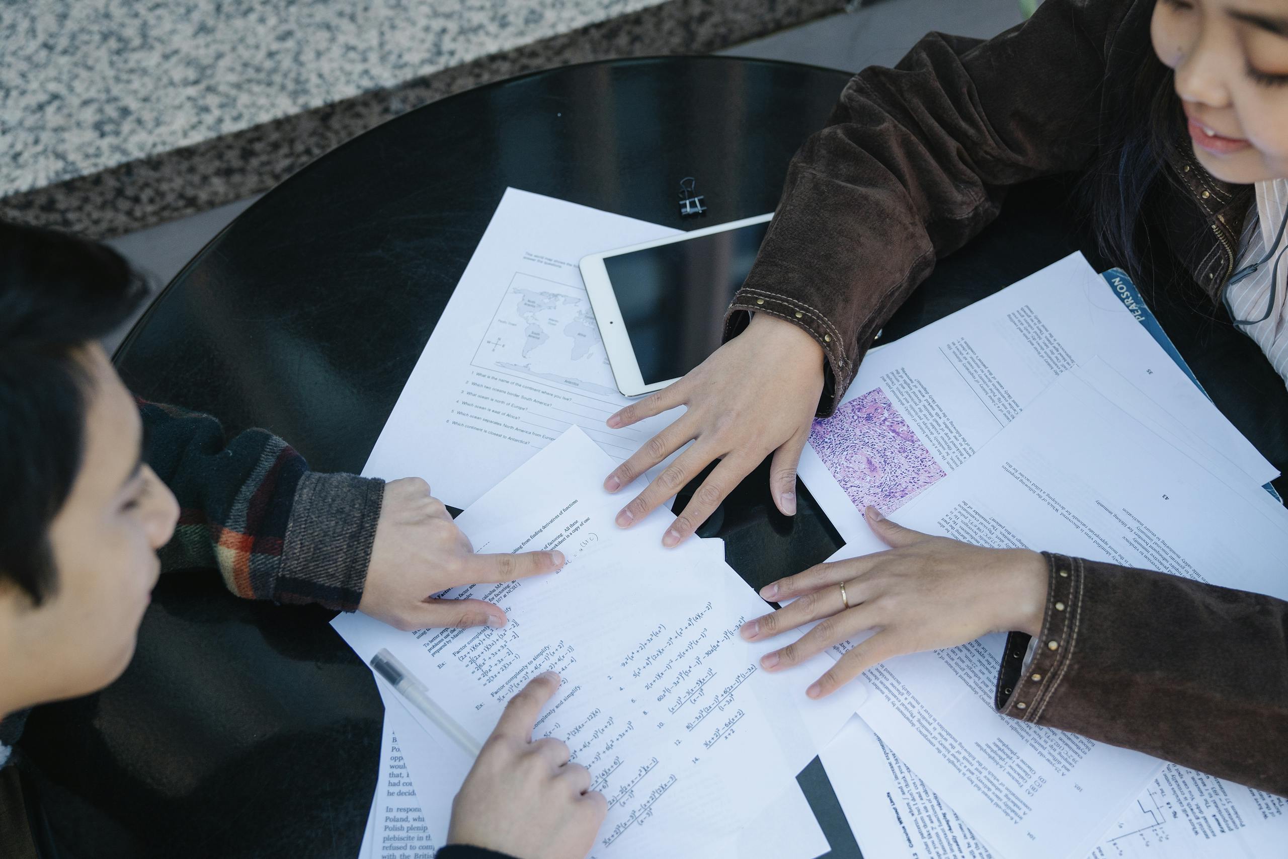 Two students discuss and study together with papers on a table, showcasing collaboration and education.